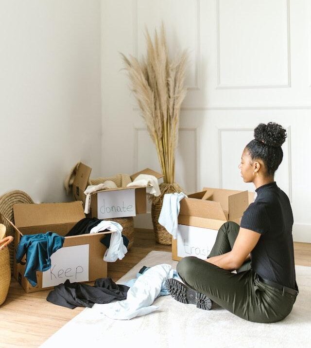 Image shows a woman sat infront of cardboard boxes labelled 'keep' donate' and 'trash' for the blog on mastering decluttering.