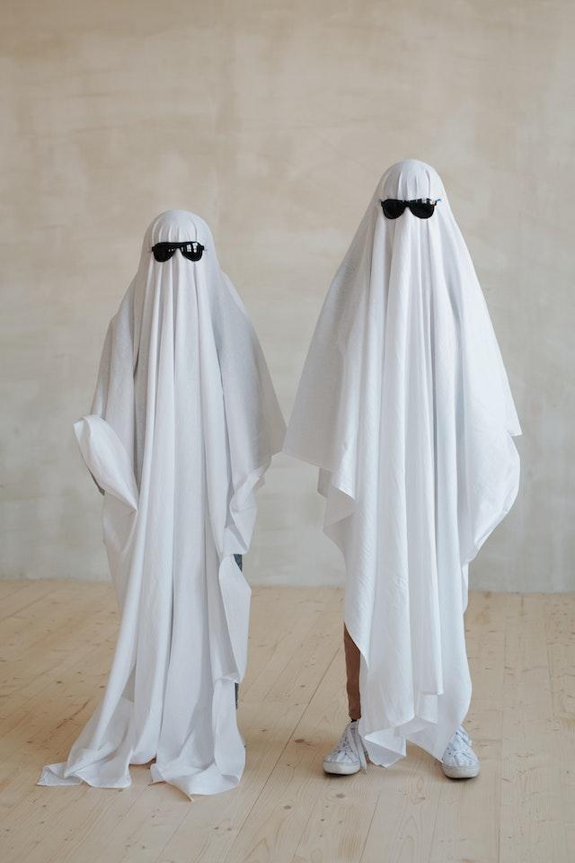 Image shows two people using sheets to dress up as ghosts wearing sunglasses as part of the blog How to Have a Hassle-Free Halloween