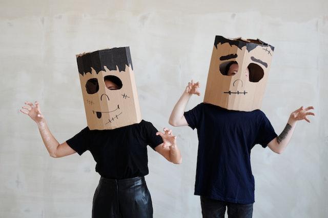 Image shows two people wearing dark clothes and cardboard boxes on their heads with eyeholes cut out and basic drawing of Frankenstein’s Monster as part of How to Have a Hassle-Free Halloween