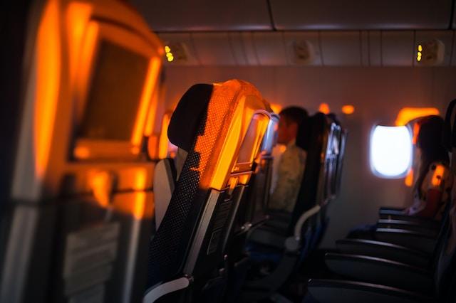 Image shows the inside of an airplane, lit by the orange hue of the setting sun to illustrate the blog on Long-Haul Flight Tips for Ultimate Comfort, Rest, and Entertainment