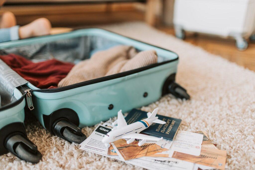 Image shows a mint hardshell suitcase open on a soft rug with two items thrown into the case.