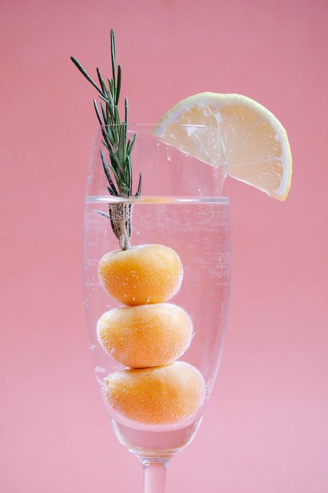 Image shows a clear cocktail in a champagne flute garnished with fig, rosemary and lemon