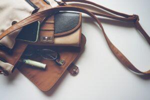 Image shows essential items for handbag including a purse, pen and glasses.