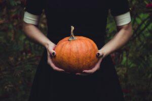 Image shows a person in a black dress holding a pumkin as part of the blog on a hassle-free Halloween.